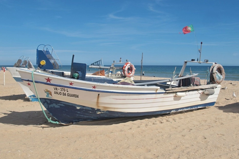 Scenic view of fishing boat and clear blue sky on Monte Gordo beach in Faro, Algarve, Portugal.