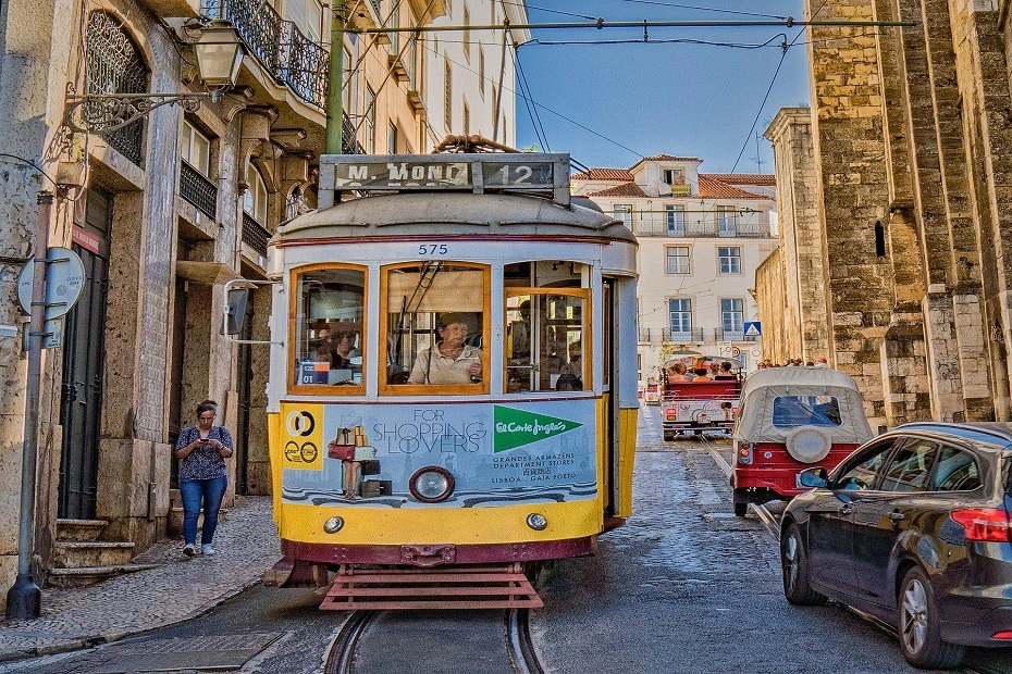 Yellow vintage tram navigating the streets on a sunny day in Lisbon, Portugal.