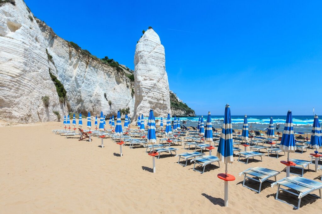The Pizzomunno monolith with beachside beds & umbrellas in Vieste, Puglia, Italy.