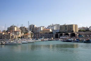 View of the marina with yachts, boats and city buildings on a sunny day in Heraklion, Crete Island, Greece.